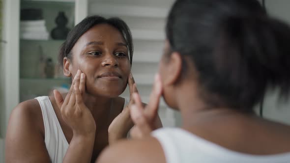 Young African-American  woman applying face cream in the mirror reflection. Shot with RED helium cam