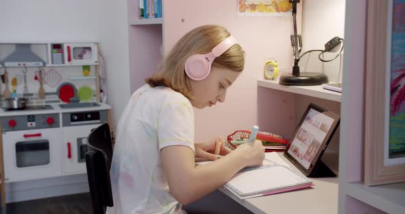 Teenager with Headphones Writes on Notebook and Uses Tablet Gadget for Internet