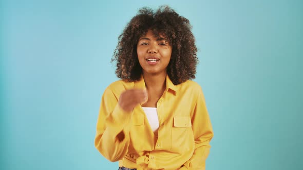 Young Darkskinned Woman Laughing and Showing Delicious Hand Gesture While Posing Against Blue Studio