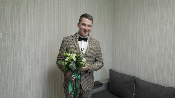 Groom with Wedding Bouquet in His Hands at Home. White Shirt, Jacket