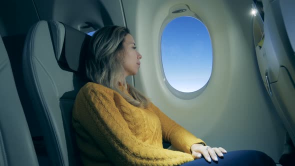 A Woman Is Looking Through the Aircraft Window. Girl Using Laptop While Is Sitting in Airplane