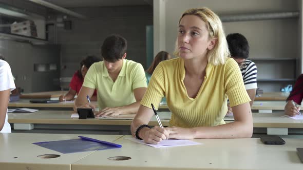 Young Blond Girl Listening to a Lecture and Writing Notes in a Classroom