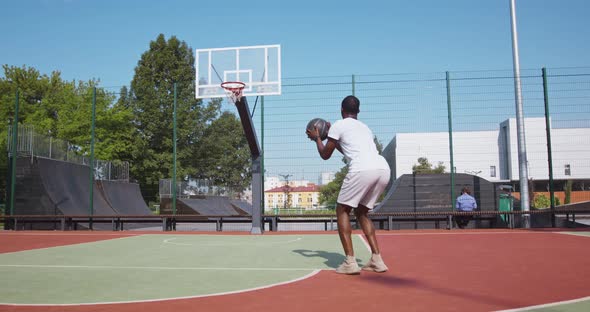 Professional Black Streetball Player Throwing Ball Into Basketball Hoop at Outdoor Court