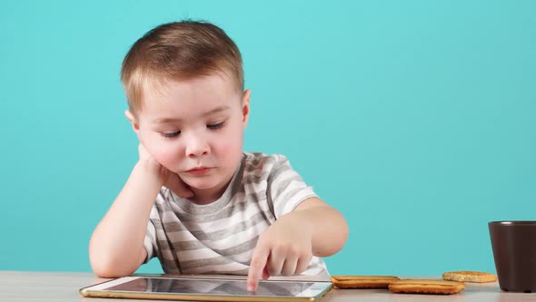 Close Up Serious Face Cute Little Child Uses a Tablet PC Sitting at Table, Isolated on Blue