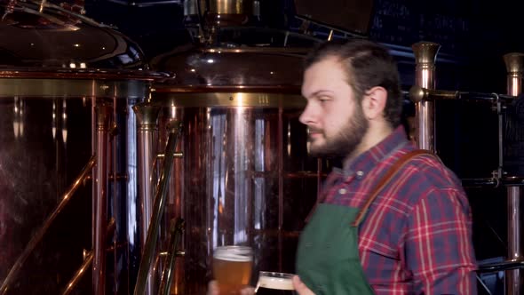 Happy Male Brewer in Apron Smiling Joyfully Holding Two Glasses of Craft Beer