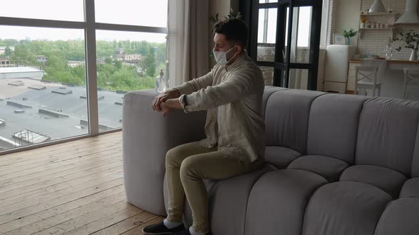 A handsome man in a protective mask carefully disinfects his hands with antiseptic