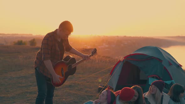 Happy Guy Plays Guitar to Friends Sitting Near Blue Tent