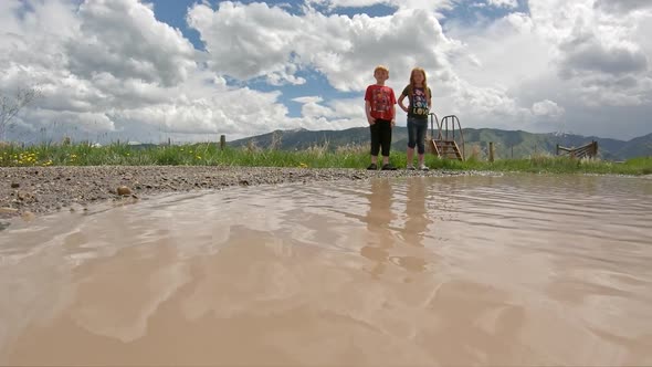 Slow motion of country kids watching rocks splash in muddy water