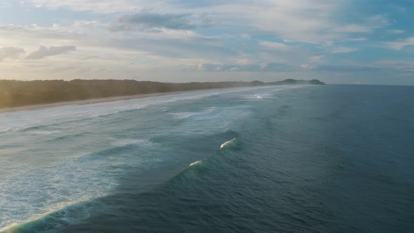 Aerial view of waves, drone flying over wide coastal sea shore area with mountain landscape in dista