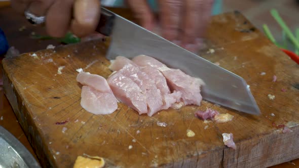 Cutting raw chicken breast on wooden board for Tom Kha Kai soup preparation