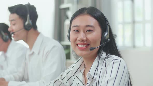 A Woman Of Three Asian Call Centre Agents Look Up From The Computer And Smile To Camera