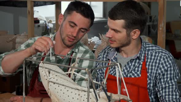 Two Male Sculptors Decorating Statue at Their Workshop