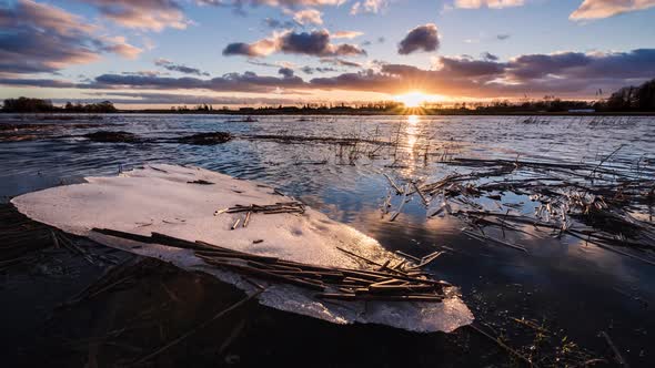 A piece of cracked ice on a shore of flooded spring river in a view of sunset sky