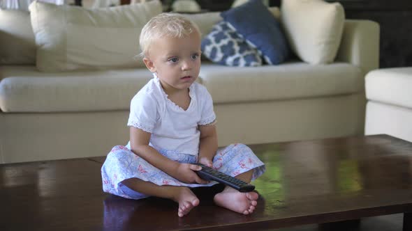 A Caucasian Toddler Girl Sitting on the Floor Watching the Tv with Remote Control