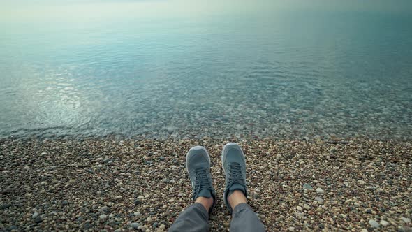 POV First Person View of Mans Legs at Pebble Sea Beach with Waves Rolls on Shore