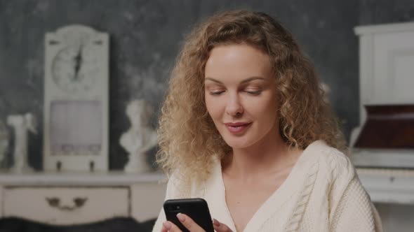 Young Curly Caucasian Woman Typing on Her Smart Phone