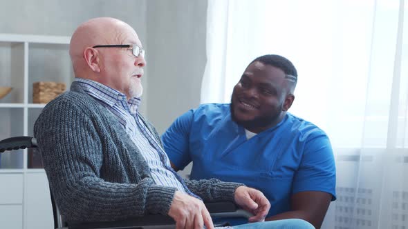 African-American caregiver and old disabled man in a wheelchair. Nurse and handicapped patient.