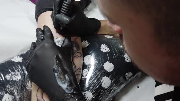 Crop tattoo master doing contour on leg of customer