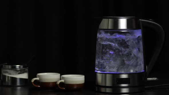 Boiling Water in Glass Transparent Electric Kettle with Blue Light Illumination. Black Background