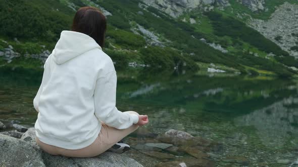 Young Woman Meditating on the Lakeshore with Amazing View on the Waterfall and Mountains. 