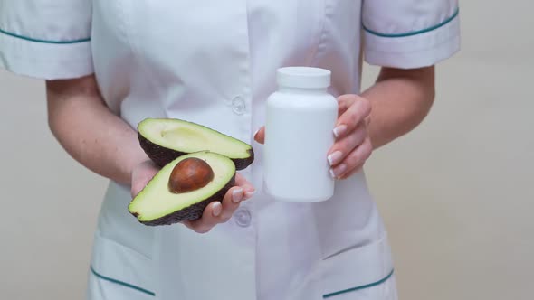 Nutritionist Doctor Holding Organic Avocado Fruit and Jar of Medicine or Vitamin or Omega 3 Capsules