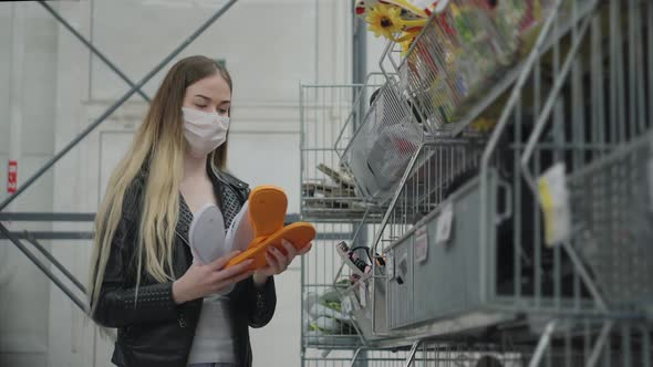 Young Lady in Medical Mask Buying Flipflops in a Mall