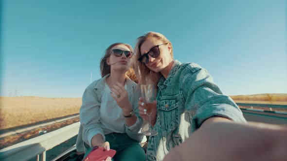 Women in Sunglasses Smile While Riding on Back of Seat of Convertible Send Kiss