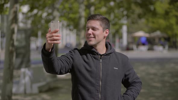 Smiling Young Man Taking Selfie with Smartphone Outdoor