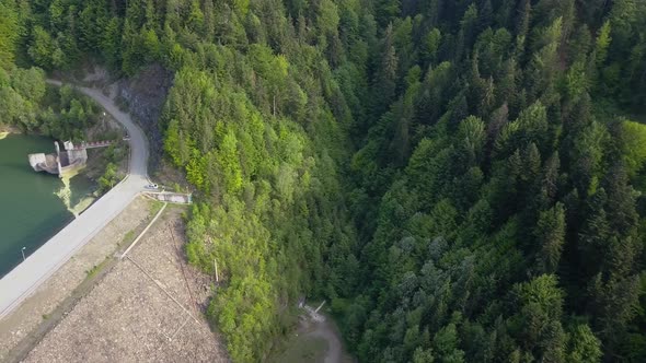 Aerial Slow Panning shot of Reservoir support with trees by the water with road running through fore