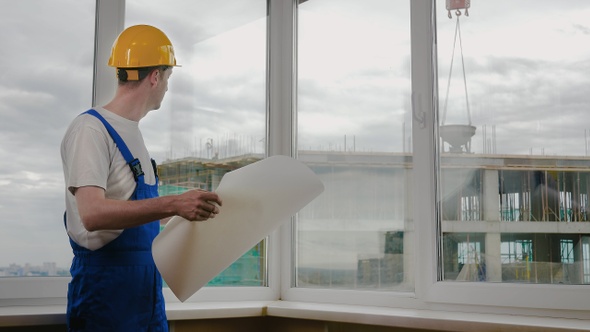 Builder at construction site with blueprint.