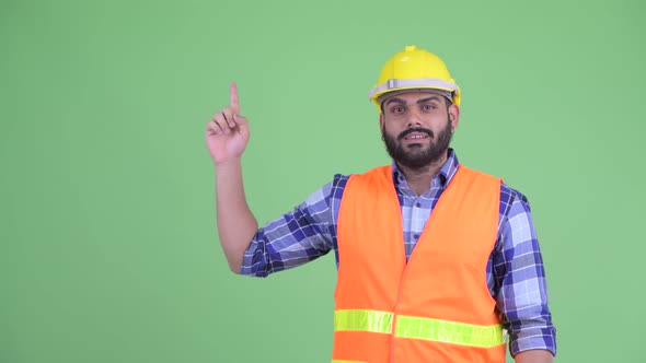 Happy Young Overweight Bearded Indian Man Construction Worker Thinking and Pointing Up