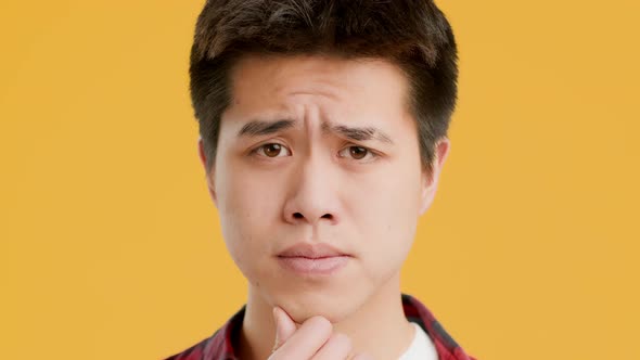 Thoughtful Asian Guy Thinking And Frowning Posing Over Yellow Background