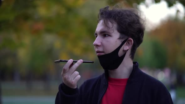 Teen with Protective Face Mask While Using Smart Phone and Sending Voice Message in the Urban Street