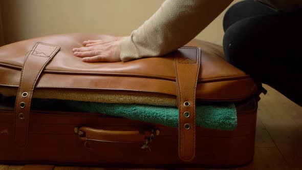 Hand trying to close stuffed over filled suitcase close up shot