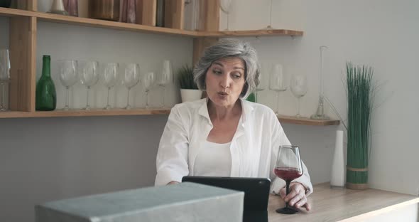 Mature Elderly 60 Year Old Woman Standing with a Tablet Drinking Wine and Enjoying Video Call