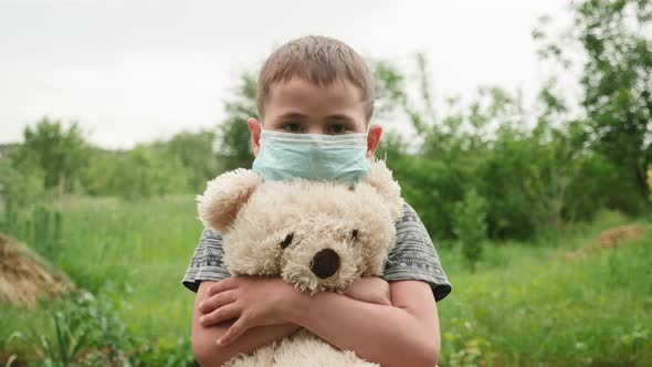 Boy child in protective medical mask looking into camera and holding teddy bear