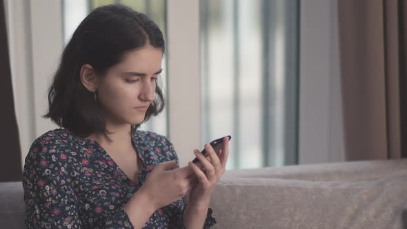 Portrait of a brunette girl with a mobile phone in her hands, window background