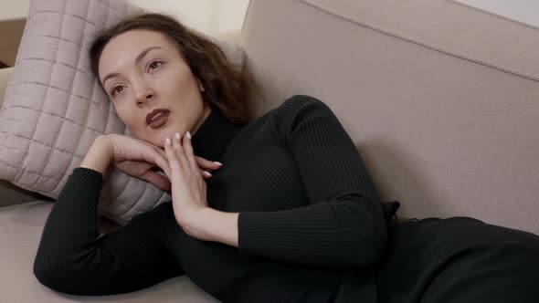 A Thoughtful Woman Lying on a Sofa on a Pillow Enjoying a Rest in a Bright Room