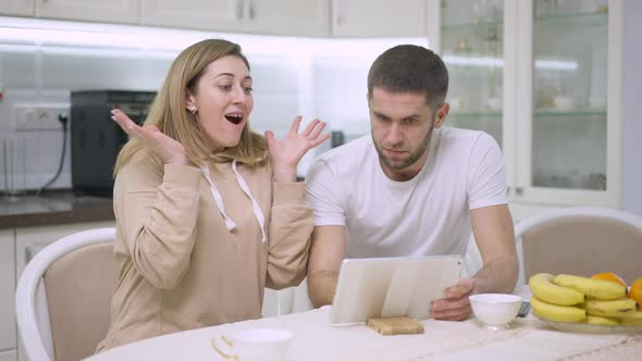 Caucasian Man and Woman Surfing Internet on Tablet Sitting in Kitchen at Home