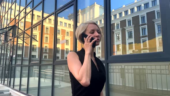 The Girl Speaks on the Phone and Walks Against the Background of a Glass Wall