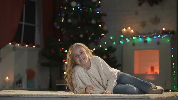 Nice Girl Lying on Floor Under Glowing X-Mas Decorations, Smiling and Having Fun