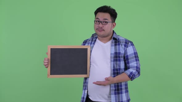 Stressed Young Overweight Asian Hipster Man Holding and Giving Thumbs Down