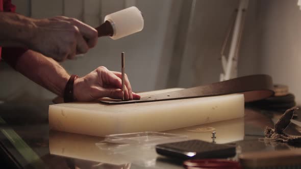 A Man Punches Holes in a Leather Belt By the Table