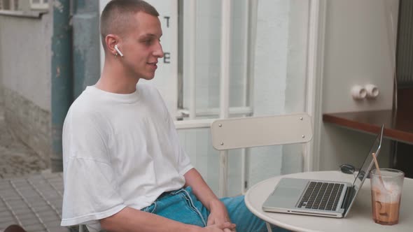 Young Caucasian Homosexual Man in Casual Outfit Sitting at Table in Cafe and Speaking Via Online