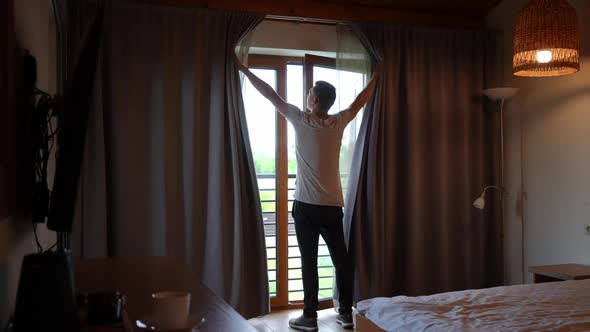 Wide Shot Back View Caucasian Young Man Opening Curtains in Hotel Room Looking Out