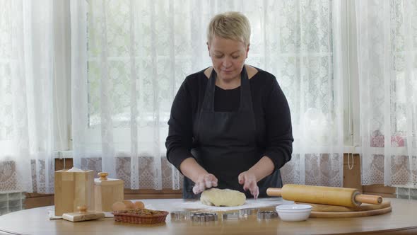Middle-aged Attractive Woman Sprinkles Flour on Table Kneads Dough Baking Pastry