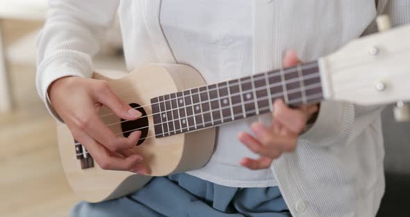 Woman play song on ukulele at home