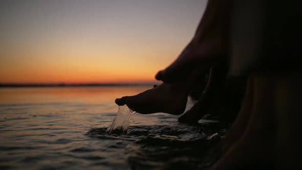 Friends Sitting at Pier Touching Sea Water with Feet at Sunrise Slow Motion