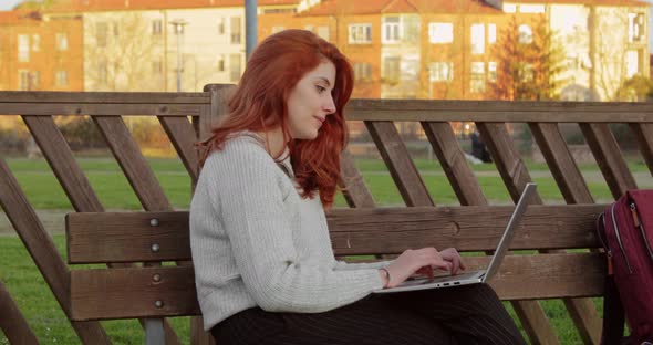 Young Female Student Working on Laptop Sitting on a Wooden Bench in a University