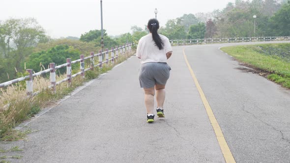 Wide shot of a fat woman running outdoors.